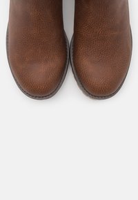 Bottes de cheville texturées marron avec des orteils arrondis, présentant un motif de grain subtil et une semelle sombre contrastante.