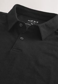 Fekete közepes méretű galléros póló két gombbal és klasszikus gallérral, "NEXT" márkajelzéssel, méretcímkével a nyakkivágás belsejében.