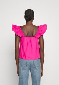 Top sin mangas fucsia con detalles de hombros con volantes, espalda elástica y cordón ajustable. Combinado con jeans de talle alto de color azul claro.