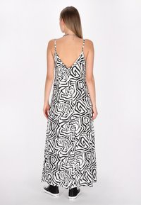 Rochie maxi cu un model abstract alb-negru, având un decolteu în V la spate, bretele subțiri și un material ușor care se desfășoară până la glezne, purtată cu adidași negri.