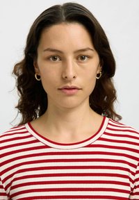 Röd och vit randig ribbad skjorta med rund halsringning. Modellen har vågigt hår och små guld hoopörhängen. Neutral bakgrund.