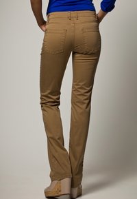 Khaki raka byxor med bakfickor, med en slät textur och en figursydd design, i kombination med ljusa högklackade skor.