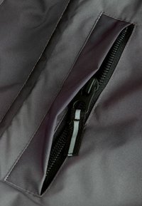 Un tissu noir avec une texture lisse présente une poche zippée, mettant en avant un zip enroulé et un tirette grise contrastante.