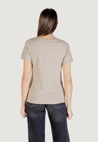 T-shirt in cotone beige con maniche corte e scollatura rotonda, mostrato da dietro. Indossato con pantaloni a gamba larga grigio scuro.