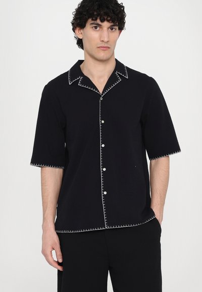 Black short-sleeve shirt with contrasting white stitching along the collar, buttons, and hem. Fabric appears soft with a relaxed fit.