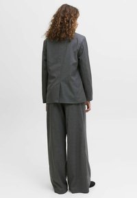 Siv vzorec obleke s prilegajočo jakno in širokimi hlačnicami. Teksturni material z rahlim karirastim vzorcem. Minimalistična oblika, pogled od zadaj.