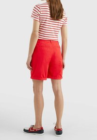 Shorts en coton rouge avec des revers, associés à un t-shirt rayé blanc et rouge. Modèle portant des chaussures bateau bleu marine et rouge.