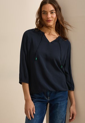 Blouse bleu marine avec décolleté en V, détails à cordon de serrage et manches trois-quarts. Fabriquée en tissu léger, avec un léger éclat et une coupe décontractée.