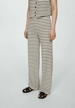 Ensemble haut sans manches rayé et pantalon large en crème et noir. Tissu texturé avec des motifs de vagues alternés. Des sandales noires complètent le look.