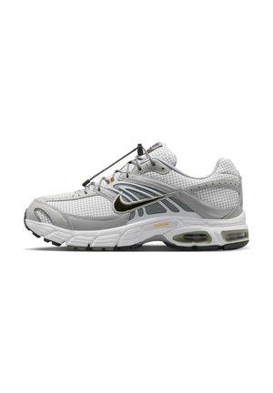 Chaussure de sport gris clair avec swoosh Nike noir, tige en mesh, semelle blanche coussinée et lacet élastique noir avec fermeture à bascule.