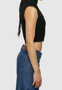 Svart ribbad crop top med hög halsringning, kombinerad med högmidjade blå denimjeans med bakfickor och en läderlapp.