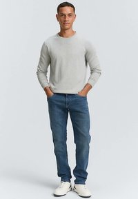 Pilkas megztinis su apvaliu kaklu, derintas su mėlynais džinsais. Džinsai yra tiesaus kirpimo su šiek tiek išblukimu; batai – balti sportbačiai.