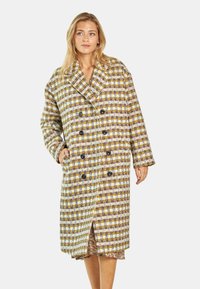 Podwójnie zapięty płaszcz w teksturowanym splocie w kolorach żółtym, brązowym i białym, z dużymi czarnymi guzikami i bocznymi kieszeniami.