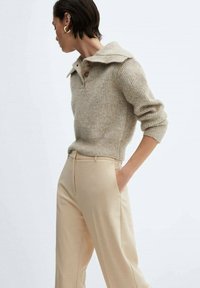 Beige wollen trui met een brede kraag en drie knopen, gecombineerd met crèmekleurige broeken met een gladde textuur en een op maat gemaakte pasvorm.