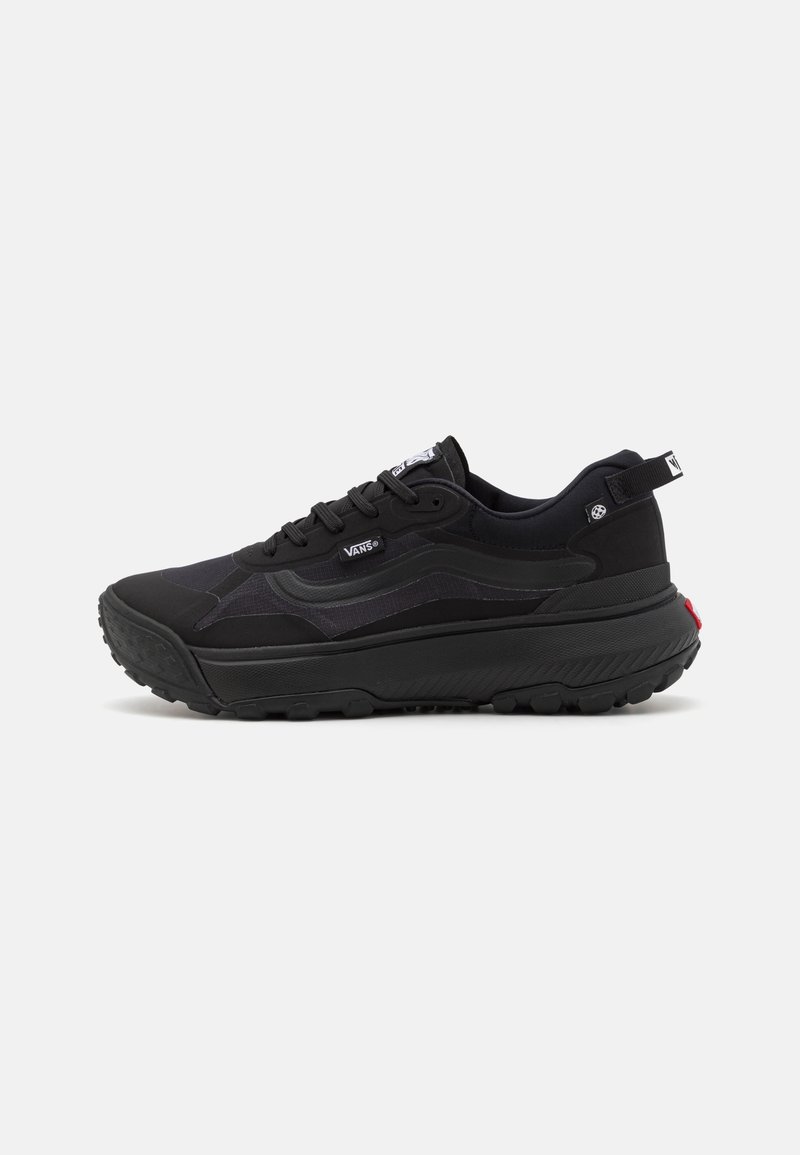 Baskets Vans noires avec semelle épaisse, lacets à l'avant, logo latéral et languette au talon sur un fond clair uni.