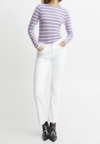 Lila och vitrandig långärmad tröja kombinerad med figursydda vita jeans. Outfiten har eleganta svarta ankelboots med dekorativa detaljer.