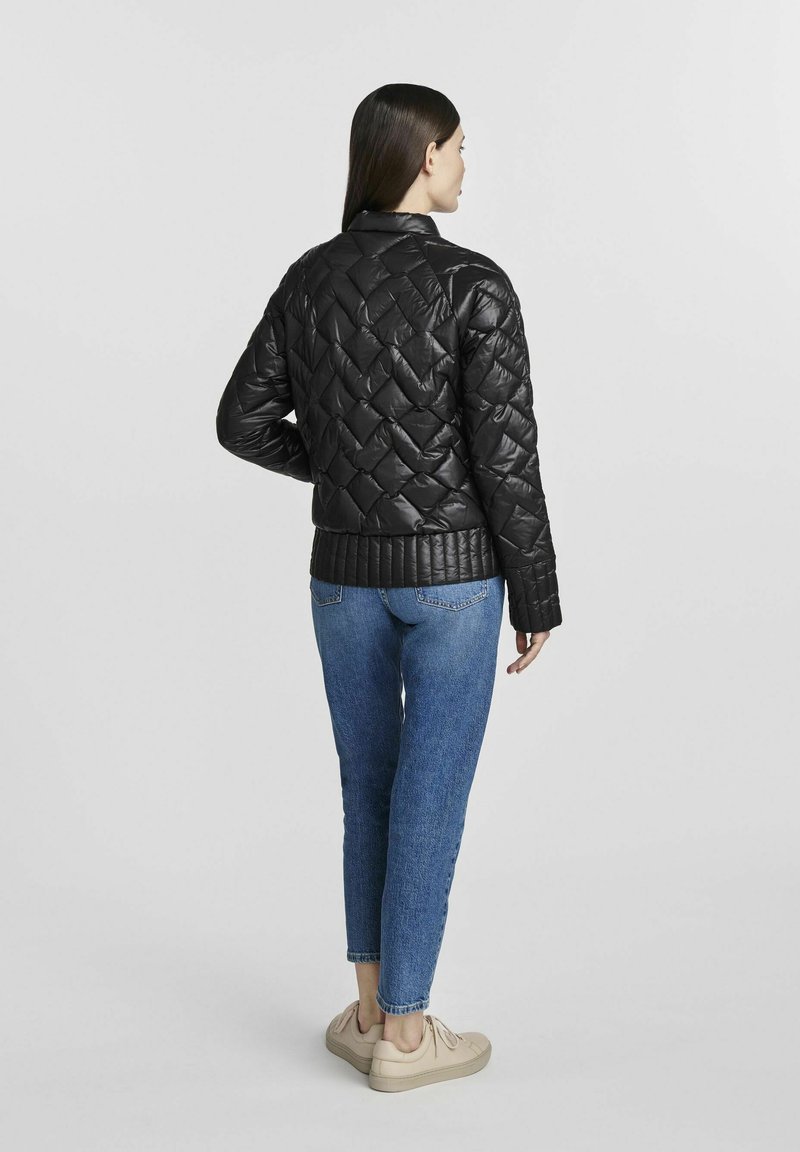 Giubbotto trapuntato nero con colletto alto, con bordo a coste. Il modello indossa jeans blu e sneakers beige, mostrato di spalle.