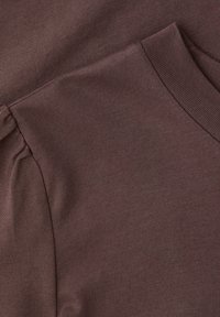 Nærbillede af brunt strikket stof, der viser ribstrikket krave og detaljer ved sammenrynket skuldersøm på et beklædningsstykke.