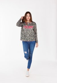 Leopard print long-sleeve top with pink "YEAH" text, paired with distressed blue skinny jeans and white sneakers.