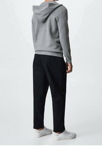 Pull à capuche gris et pantalon noir, associés à des baskets blanches. Le tissu semble doux, et la coupe est décontractée avec des détails de couture visibles.