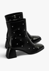 Botines de cuero negro con punta puntiaguda, tachuelas decorativas plateadas y tacón bloque. Cierre de cremallera en la parte trasera.