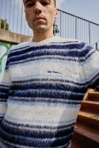 Svītrots adīts krekls ar zilām, tumši zilām un baltām krāsām, ar mīkstu tekstūru; apaļa kakla izgriezums un diskreta izšūta rakstība.