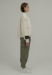 Veste blanche courte avec une finition texturée, associée à un pantalon cargo olive et des baskets blanches. Présente des accents audacieux et des étiquettes visibles.