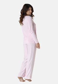 Top a maniche lunghe rosa chiaro abbinato a pantaloni da pigiama a righe rosa e bianche. Tessuto morbido con una vestibilità rilassata e orli arrotolati sulle caviglie.