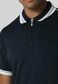 Polo navy con colletto a zip, con dettagli a strisce bianche. Tessuto morbido e testurizzato con un piccolo logo sul petto.