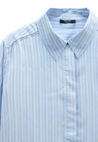 Jasnoniebieska męska koszula wyjściowa z cienkimi pionowymi białymi i granatowymi paskami oraz klasycznym kołnierzykiem, ułożona na płasko na białym tle.