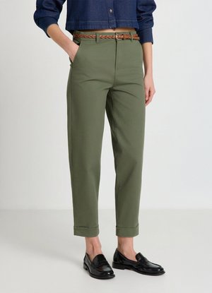 Pantalon vert olive à coupe droite, ourlets retroussés, passants pour ceinture et ceinture tressée marron. Associé à des mocassins noirs.