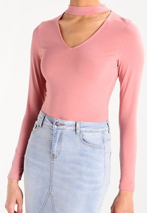 Langärmeliger, hellrosa Body mit V-Ausschnitt und Choker-Ausschnitt, kombiniert mit einem hochgeschnittenen, hellblauen Jeansrock mit Schlitz.