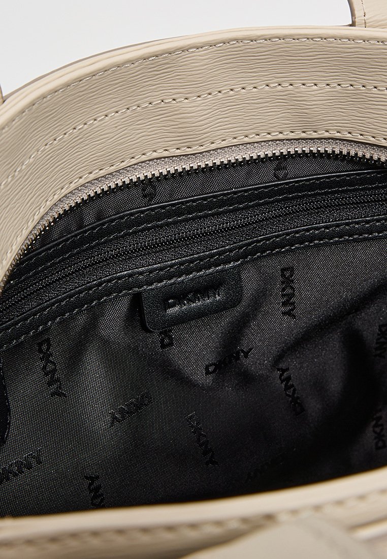 Beige synthetische Leder Tasche Innenraum mit schwarzem Stofffutter. Verfügt über eine Reißverschlusstasche mit Logo, sauberen Nähten und glatter Textur.