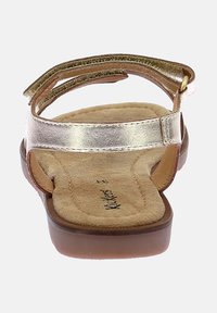 Sandales plates avec une semelle intérieure rembourrée beige, des sangles dorées métalliques et une semelle lisse brune. Dispose d'une sangle à l'arrière pour un maintien sécurisé.