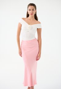Top bianco a spalle scoperte con un design torcigliato e accentuato da una rosa, abbinato a una gonna in satin rosa aderente e svasata. Texture liscia.