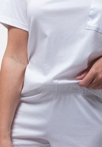 Valkoinen puuvillapaita lyhyillä hihoilla, jossa on rintatasku ja rento leikkaus. Yhdistetty samankaltaisiin joustaviin shortsit. Sujuva rakenne.