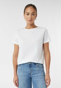T-shirt en coton blanc avec un col rond et des manches courtes, associé à un jean en denim bleu clair. Texture lisse, coupe décontractée.