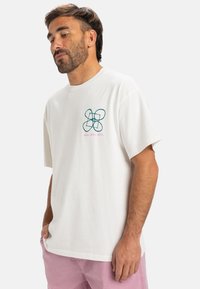 Hvid bomulds T-shirt med et turkis grafisk design af overlappende former og lyserøde accenter, med en afslappet pasform og korte ærmer.