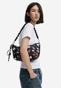 Borsa a tracolla nera intrecciata con accenti floreali colorati, una tracolla intrecciata e una forma curva; realizzata in pelle con accessori metallici.