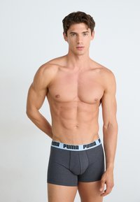 Boxeri gri cu un brâu elastic de culoare albastră deschisă, pe care este inscripționată logo-ul "PUMA", prezentati pe un model cu un fundal neutru.