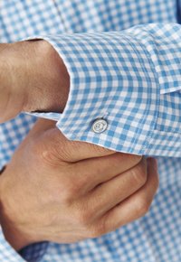 Manga de camisa de cuadros vichy en azul y blanco con un detalle de botón, que muestra una suave tela de algodón y un acabado de costura pulcro.