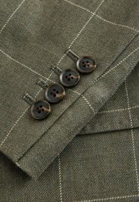 Gros plan sur quatre boutons brun foncé sur un tissu en tweed vert avec un motif quadrillé blanc cousu sur la manche d’une veste.