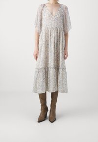 Floral-patterned, light-colored midi dress with flutter sleeves and a V-neck. Paired with brown fitted knee-high boots.