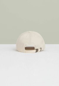 Beige bomulds cap med en struktureret ryg. Har en forstærket knap på toppen og en justerbar rem med en metalspænde.