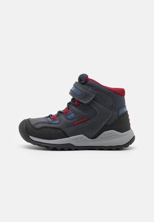 Bottes de randonnée grises de hauteur moyenne avec des accents rouges et bleus, des sangles à boucle et velcro, une semelle en caoutchouc, un tissu texturé et une coque de protection renforcée.