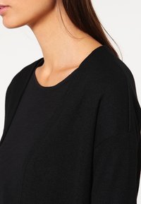 Svart kofta med en texturerad stickad mönster, öppen frontdesign och korta ärmar. Tillverkad av mjukt material, lämplig för lager-på-lager.