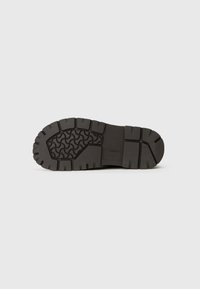 Suela de zapato de goma negra con un patrón de agarre texturizado, que presenta ranuras profundas y una construcción robusta para proporcionar tracción y durabilidad.