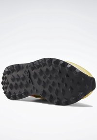 Semelle extérieure en caoutchouc noir avec des crampons adhérents agressifs ; talon bas, bout arrondi et semelle intermédiaire jaune avec des détails d'accent lumineux le long du bord.