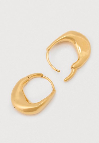 Kuldtooni rõngasukad orgaanilise, voolava kujuga ja läikiva pinnaga. Omavad kerget ulatust asümmeetrilise disaini jaoks.