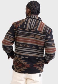 Wollen jasje met patroon in aardetinten, met geometrische ontwerpen, een kraag en lange mouwen. Gestructureerde stof met een warme uitstraling.